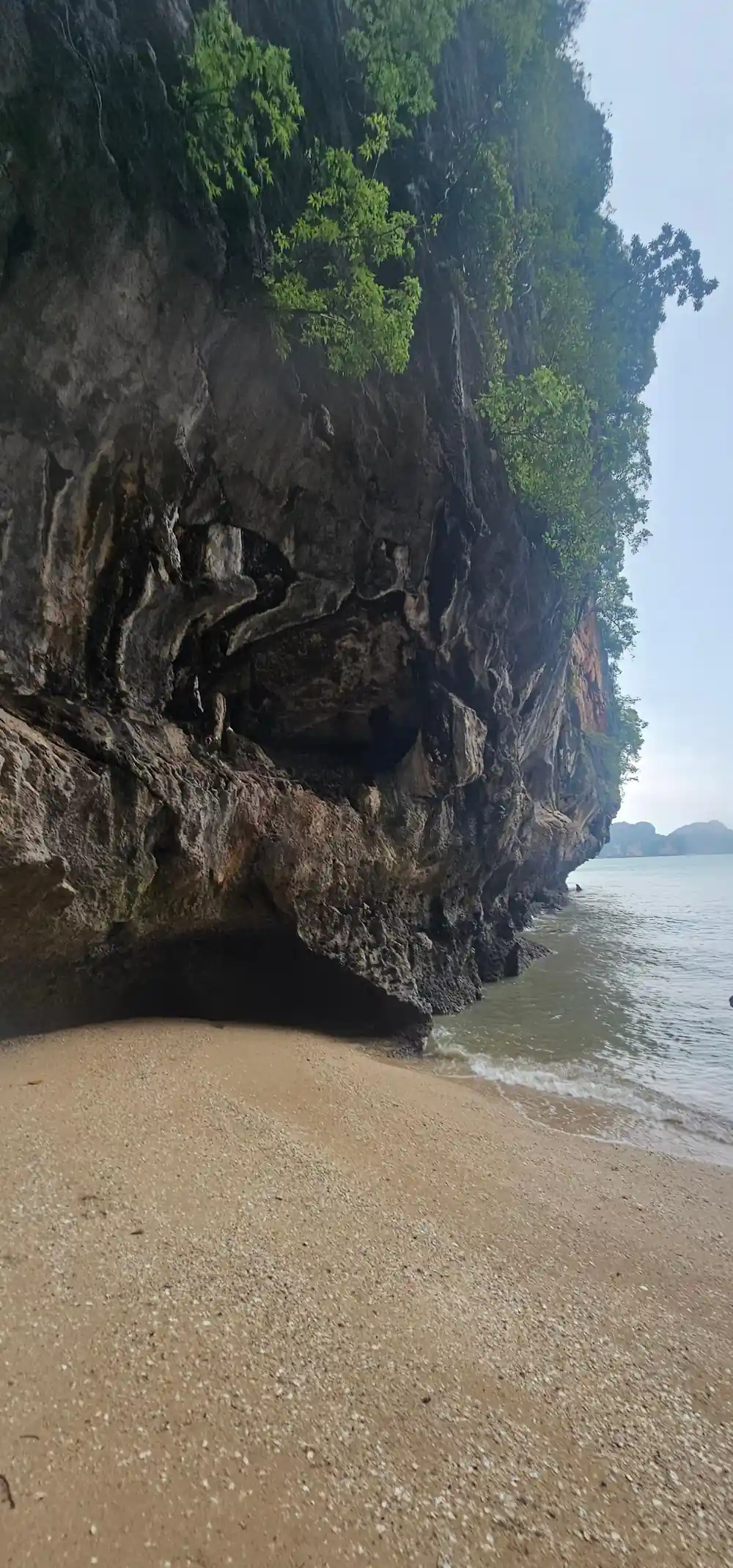 Cave opening in limestone cliff above sandy beach