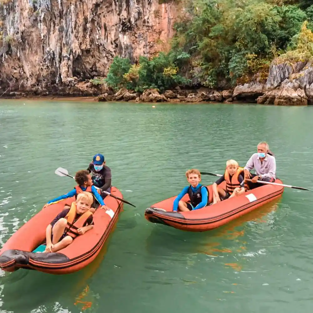 Family groups in orange boats on turquoise water near cliff