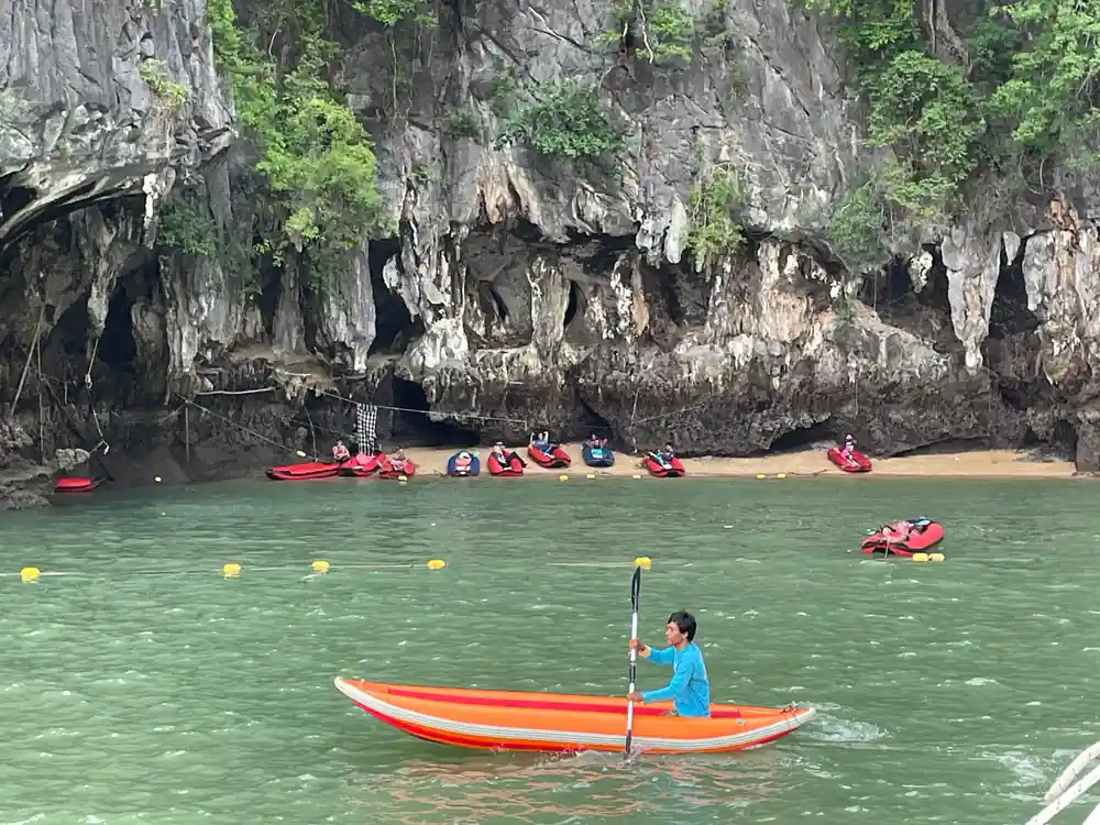 Multiple kayakers and paddleboarders beneath massive cave overhang