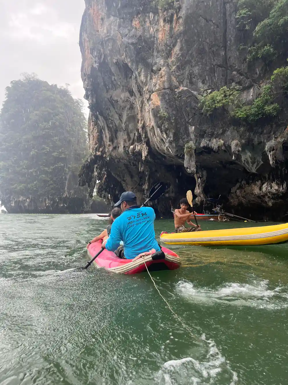 Person in kayak paddling near large limestone cliff overhang