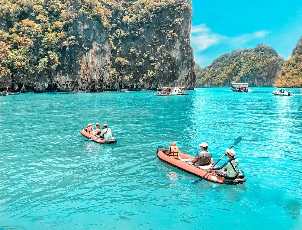 Red and orange kayaks near limestone cliffs and boats
