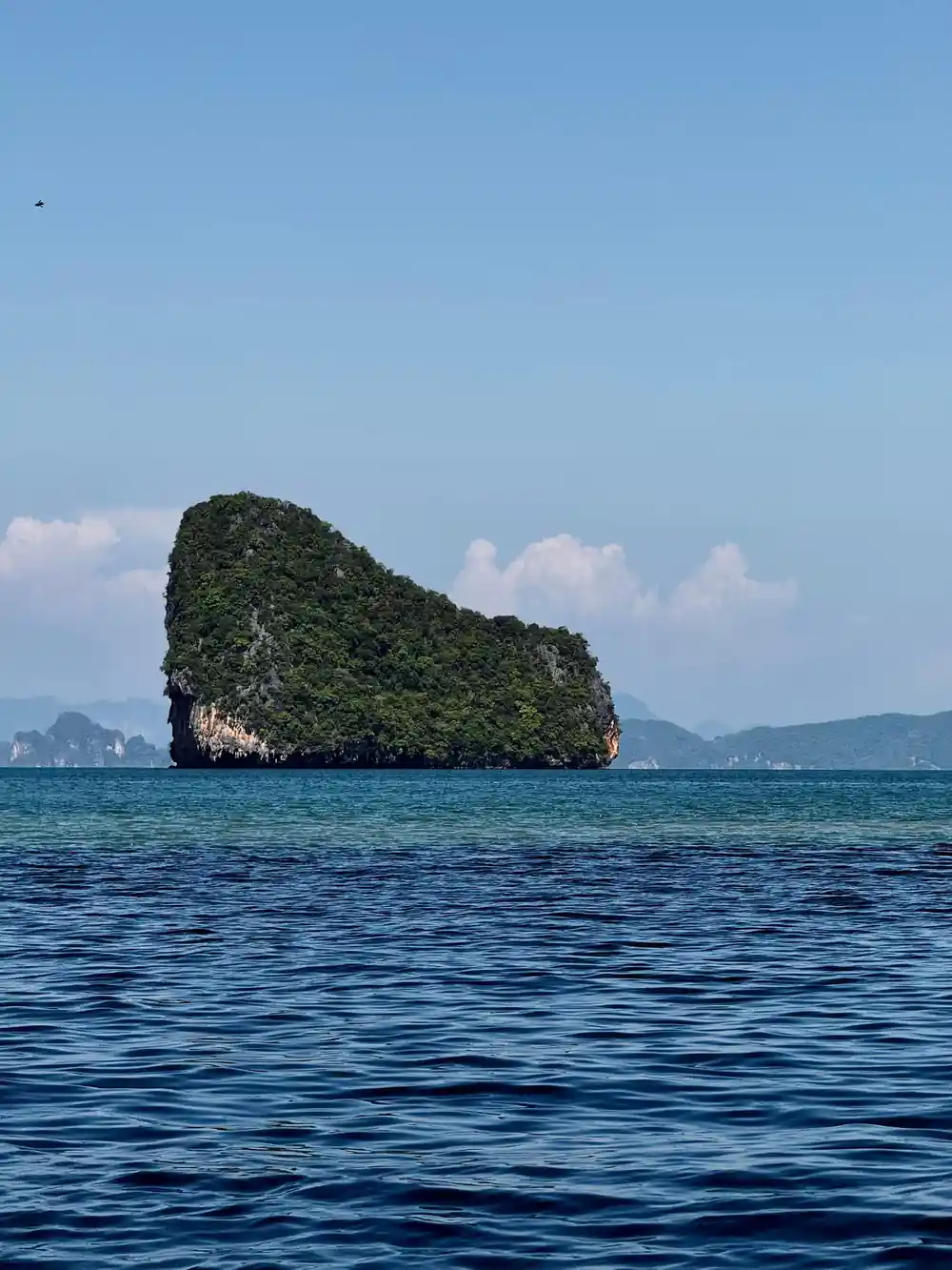 Single vegetated limestone island rising from blue water