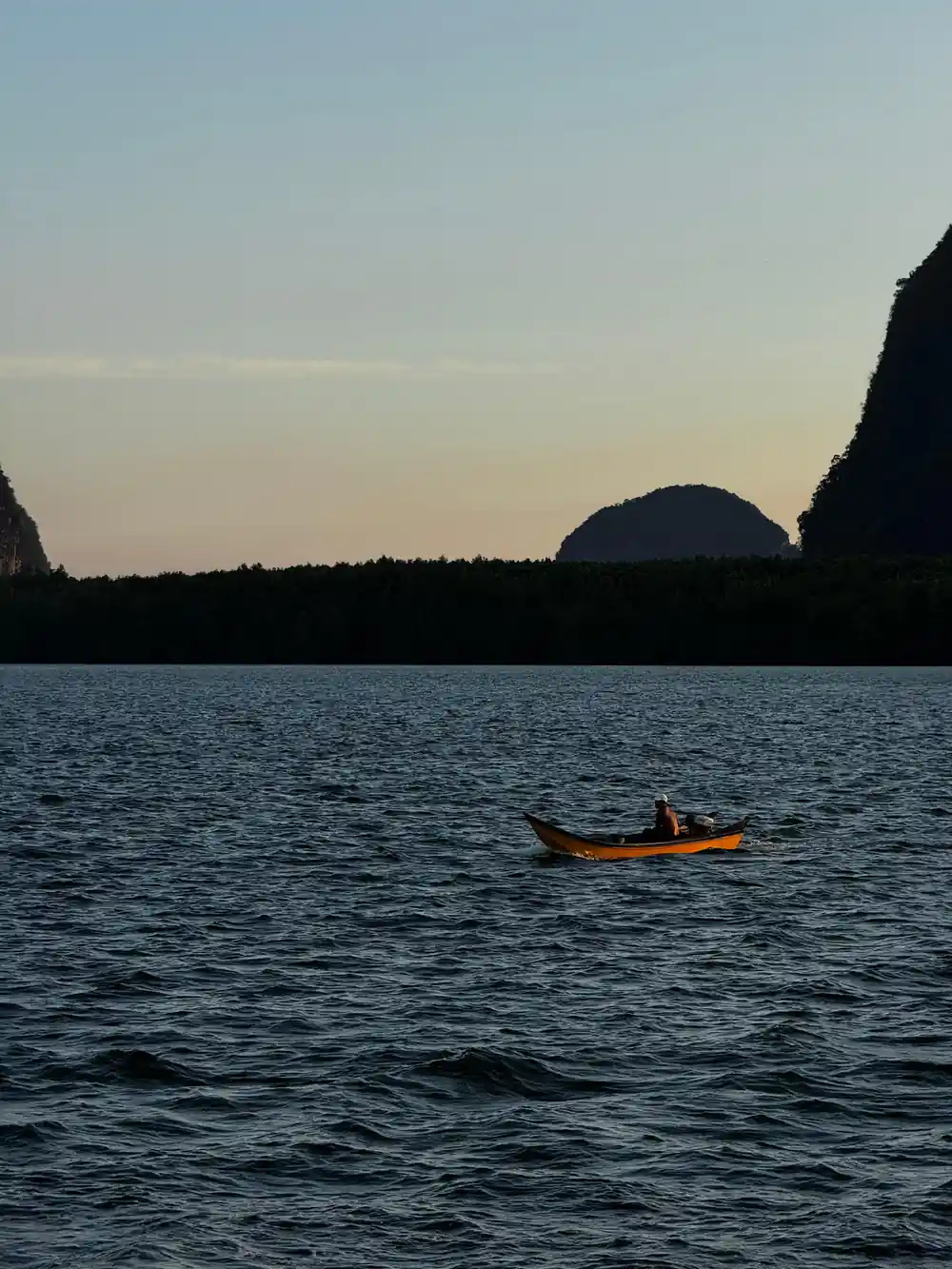 Small boat on calm water between tall limestone cliffs