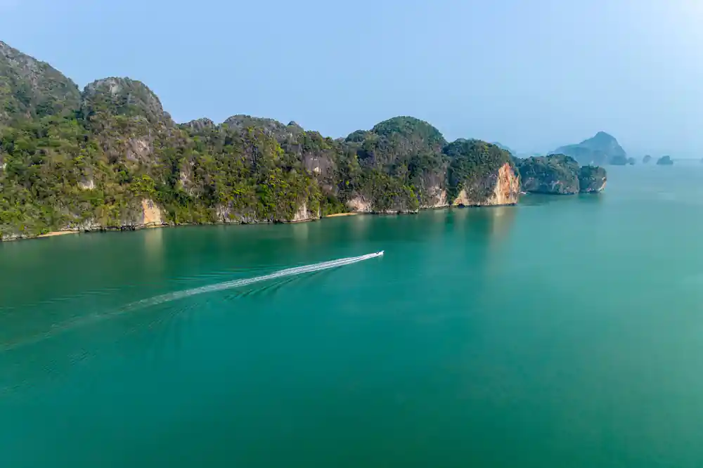 Speedboat cruising past limestone islands in emerald water