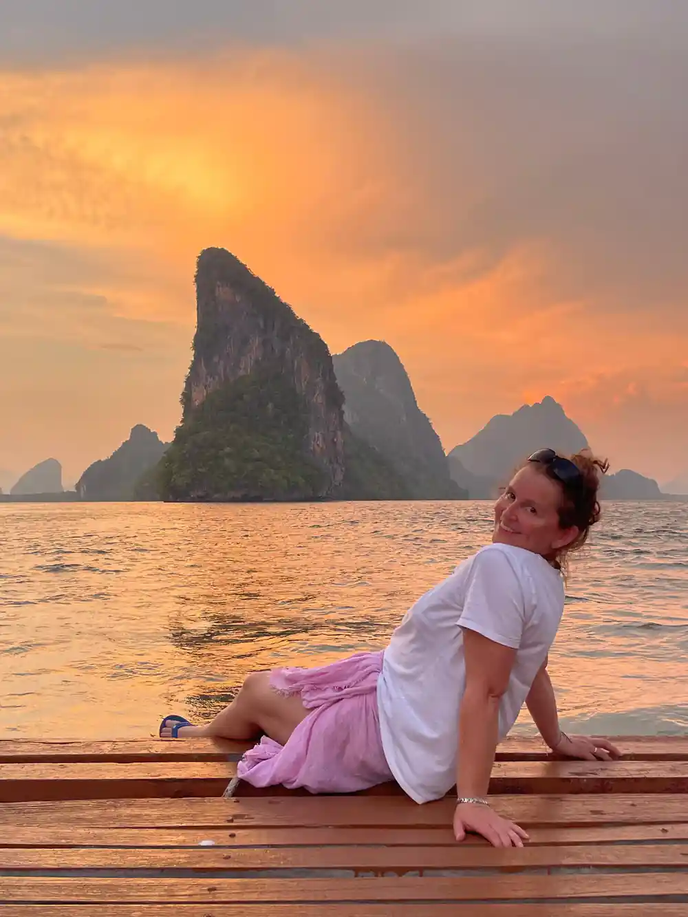 Woman posing on wooden boat deck at sunset with karst islands
